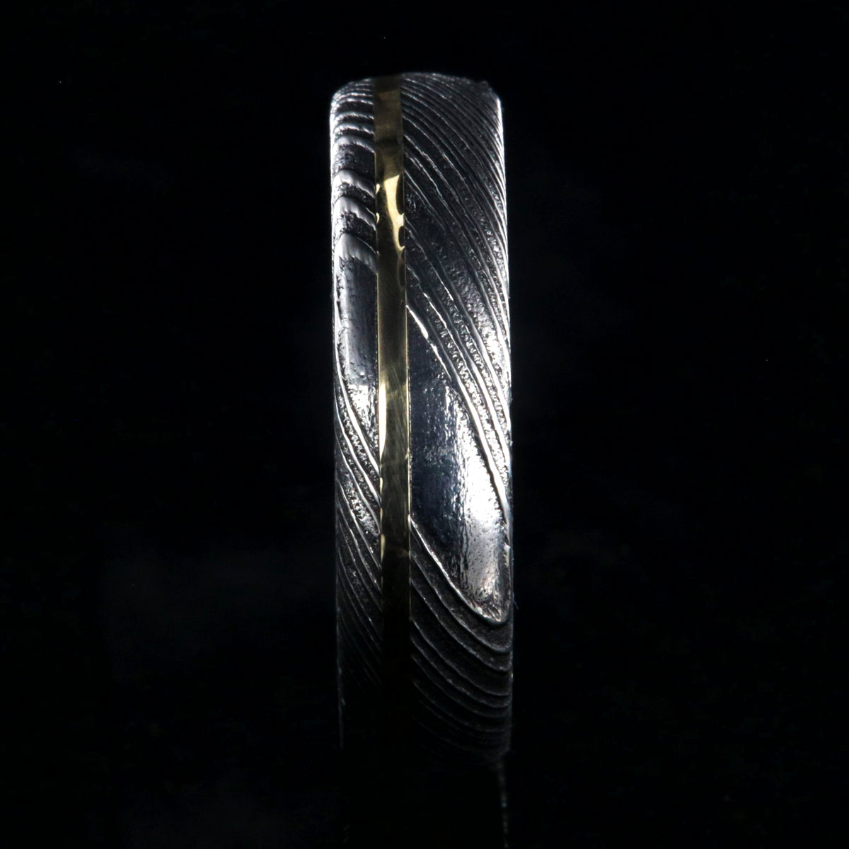 6mm wide black Damascus steel ring with polished inside and a thin off-center yellow gold inlay