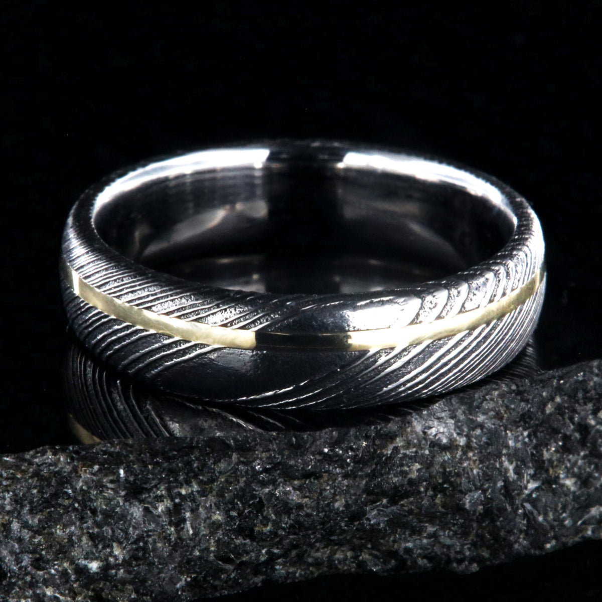 6mm wide black Damascus steel ring with polished inside and a thin off-center yellow gold inlay