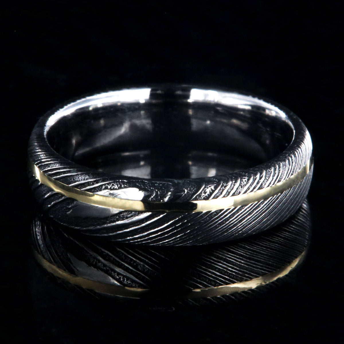 6mm wide black Damascus steel ring with polished inside and a thin off-center yellow gold inlay
