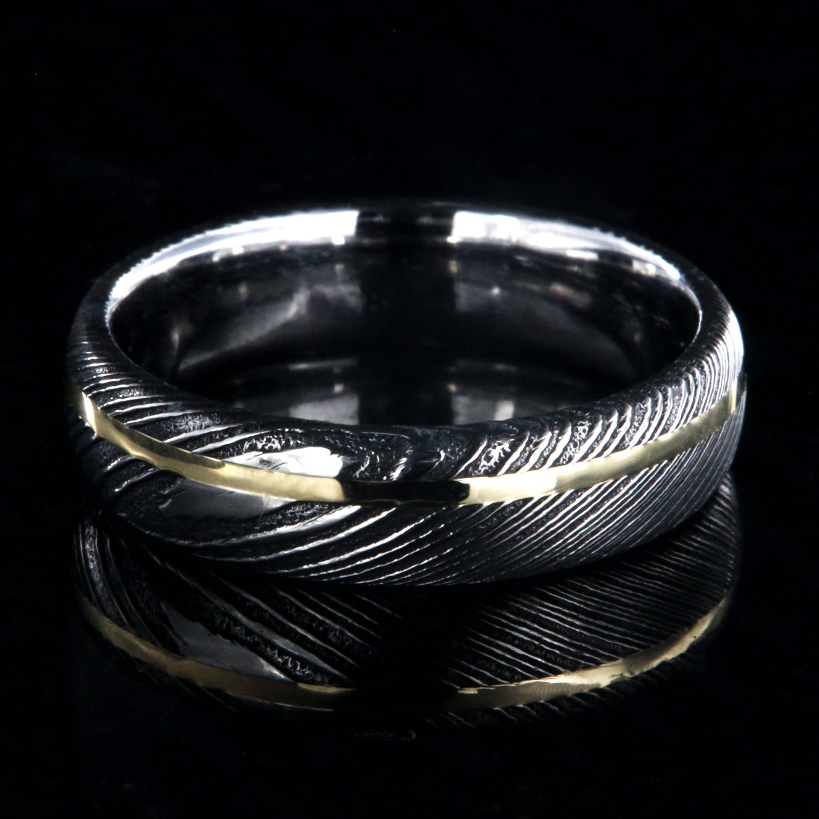 6mm wide black Damascus steel ring with polished inside and a thin off-center yellow gold inlay