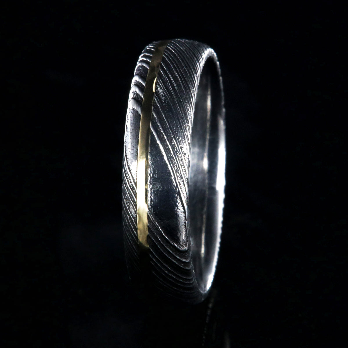 6mm wide black Damascus steel ring with polished inside and a thin off-center yellow gold inlay