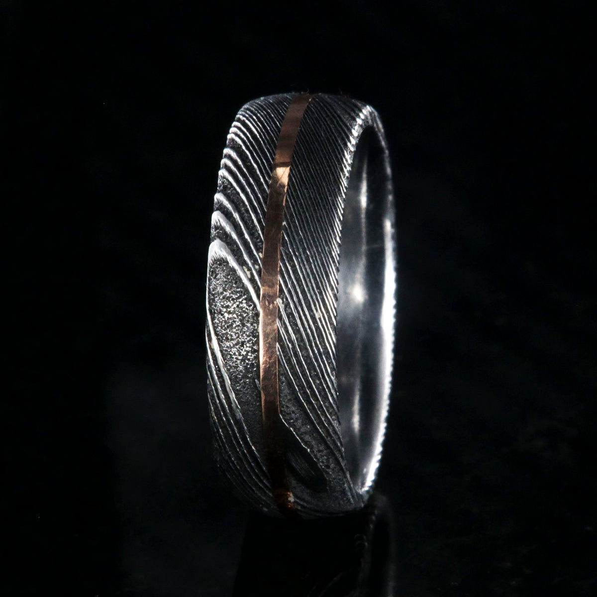 7mm wide black Damascus steel men&#39;s wedding band with centered rose gold inlay and polished inside