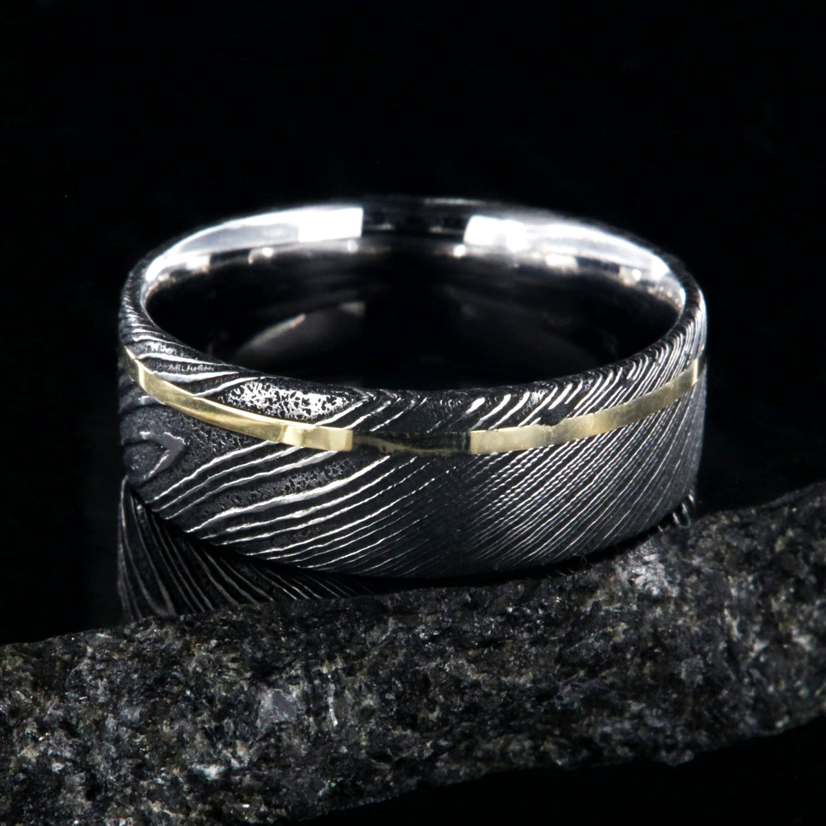8mm wide black Damascus steel ring with a flat profile, polished inside, and a thin off-centered rose gold inlay