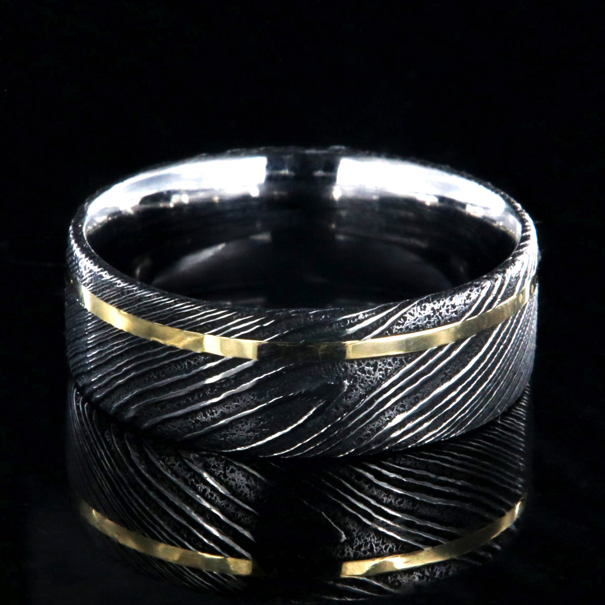 8mm wide black Damascus steel ring with a flat profile, polished inside, and a thin off-centered rose gold inlay