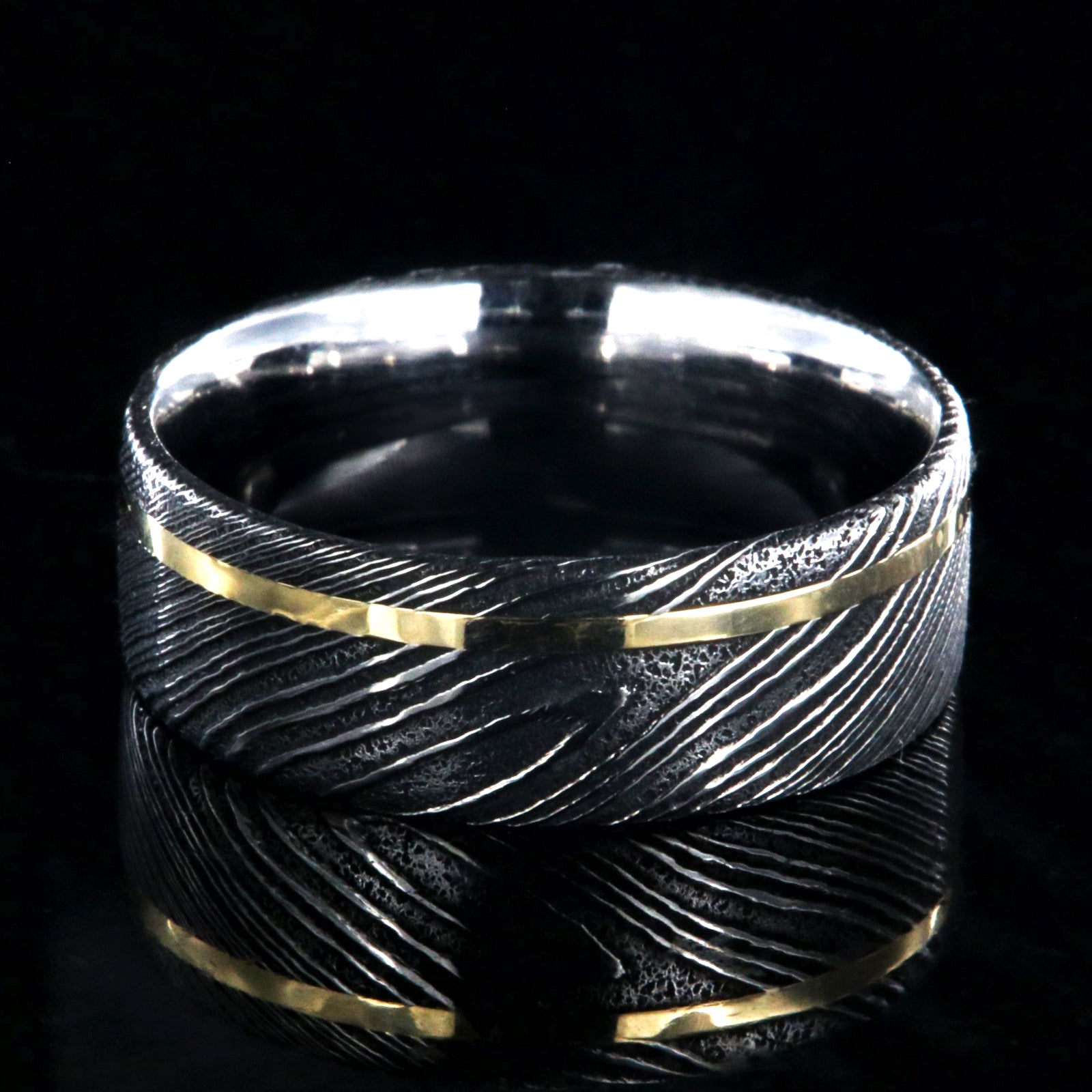 8mm wide black Damascus steel ring with a flat profile, polished inside, and a thin off-centered rose gold inlay