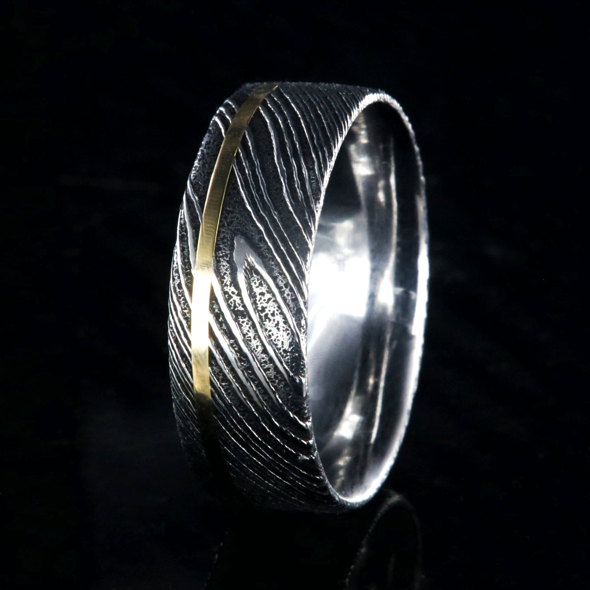 8mm wide black Damascus steel ring with a flat profile, polished inside, and a thin off-centered rose gold inlay