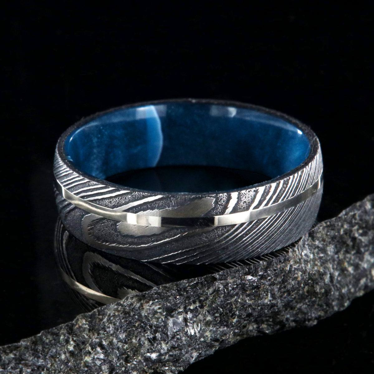 8mm wide black Damascus steel ring with a swirled blue acrylic sleeve and white gold inlay
