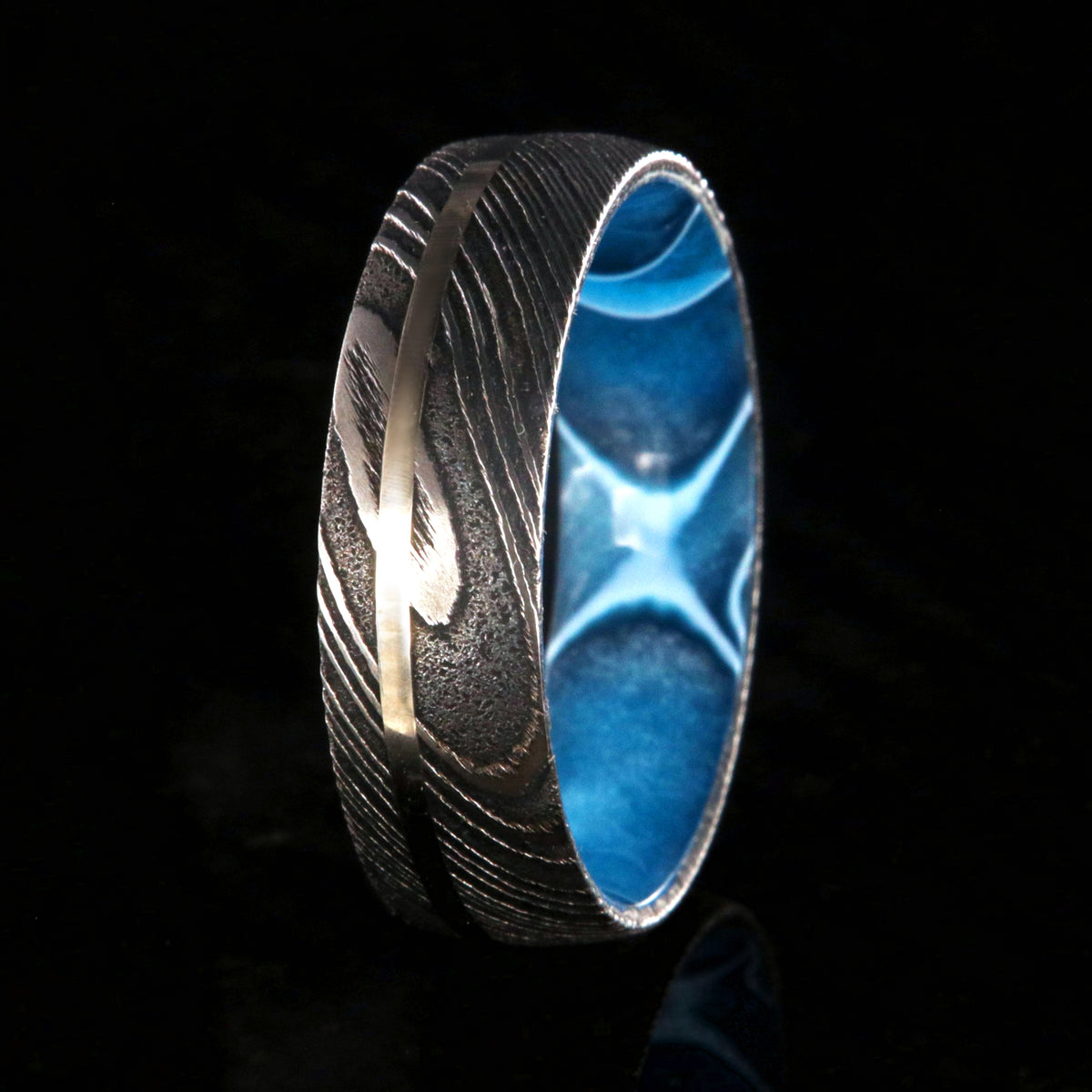 8mm wide black Damascus steel ring with a swirled blue acrylic sleeve and white gold inlay