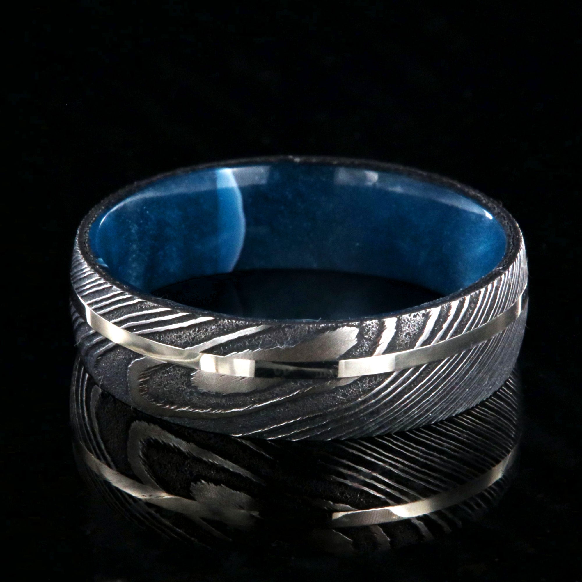 8mm wide black Damascus steel ring with a swirled blue acrylic sleeve and white gold inlay