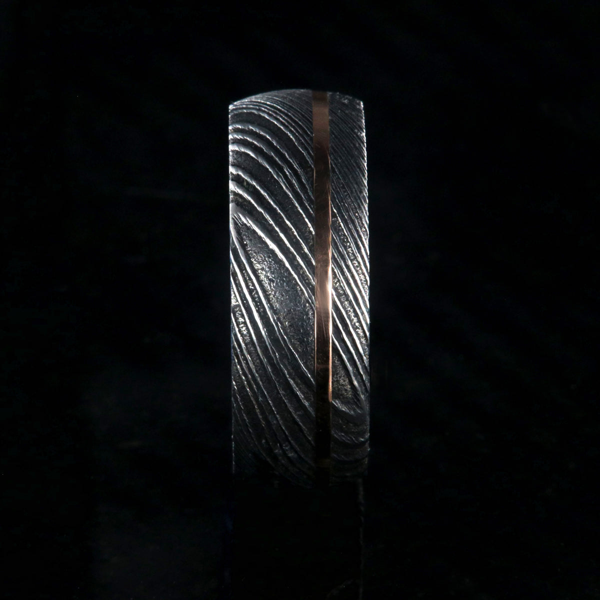 8mm wide black Damascus steel ring with an off-center rose gold inlay and dark blue acrylic sleeve