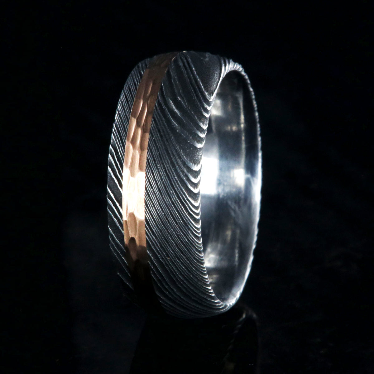 8mm wide black Damascus steel wedding band with a wide rose gold inlay with hammered finish and polished inside