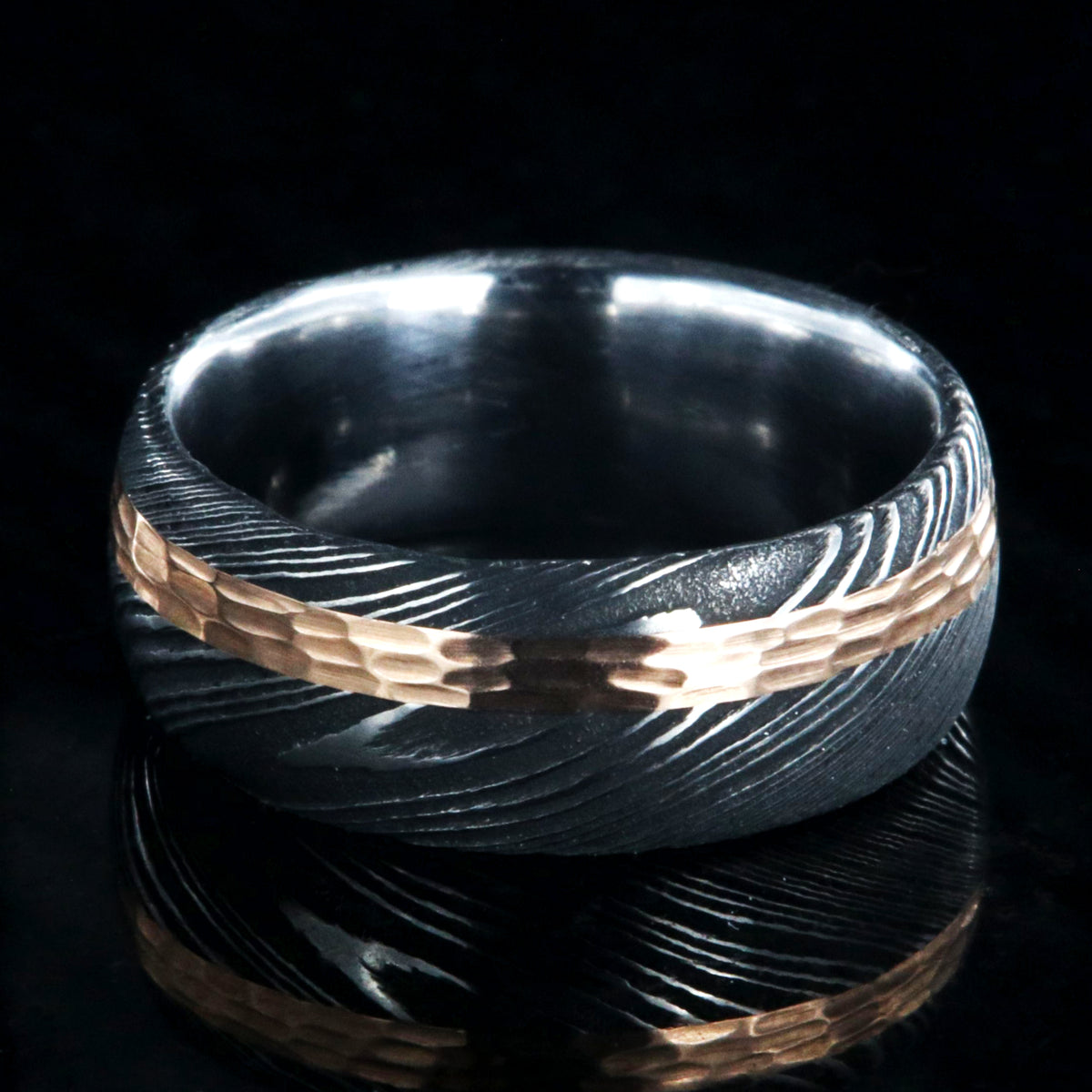 8mm wide black Damascus steel wedding band with a wide rose gold inlay with hammered finish and polished inside