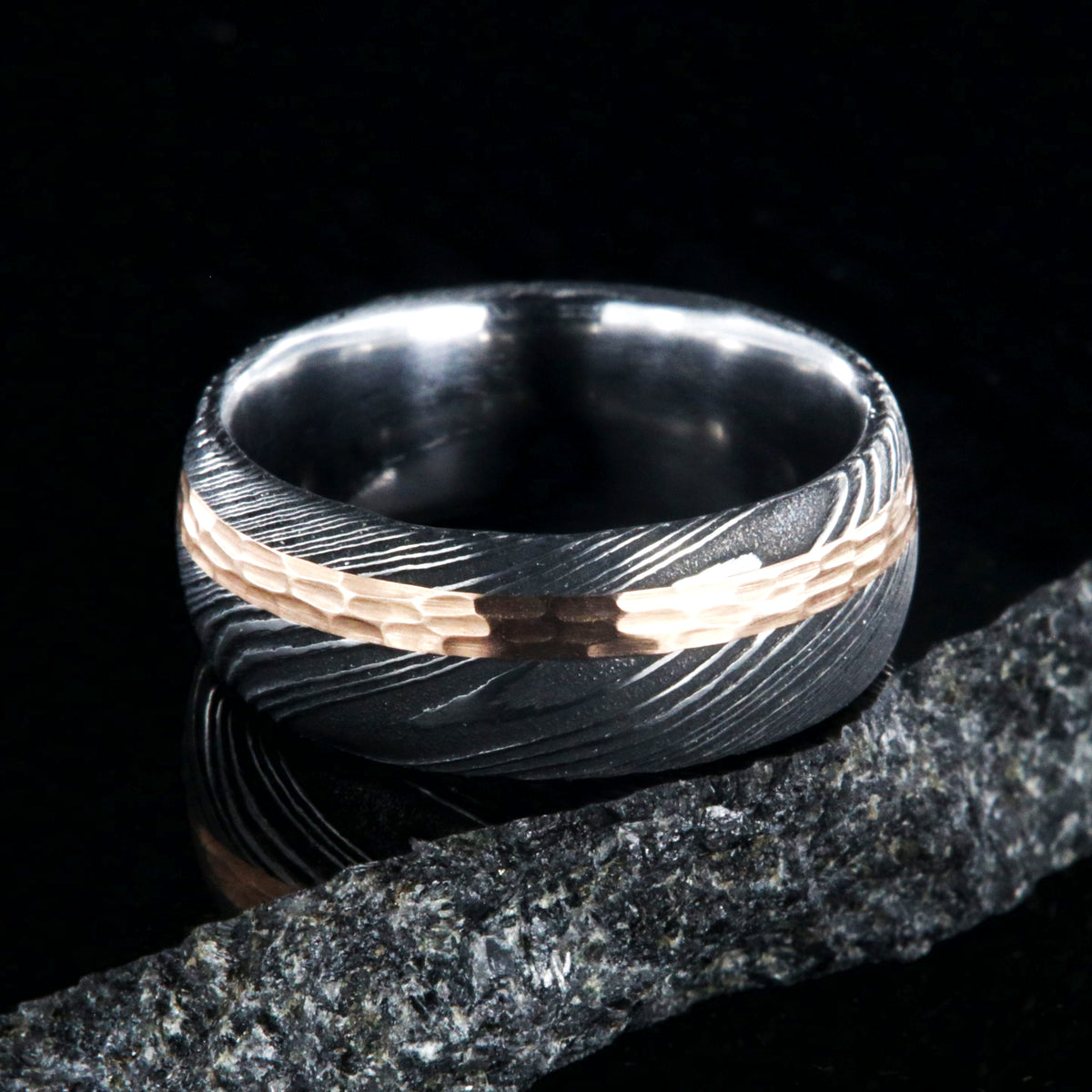 8mm wide black Damascus steel wedding band with a wide rose gold inlay with hammered finish and polished inside