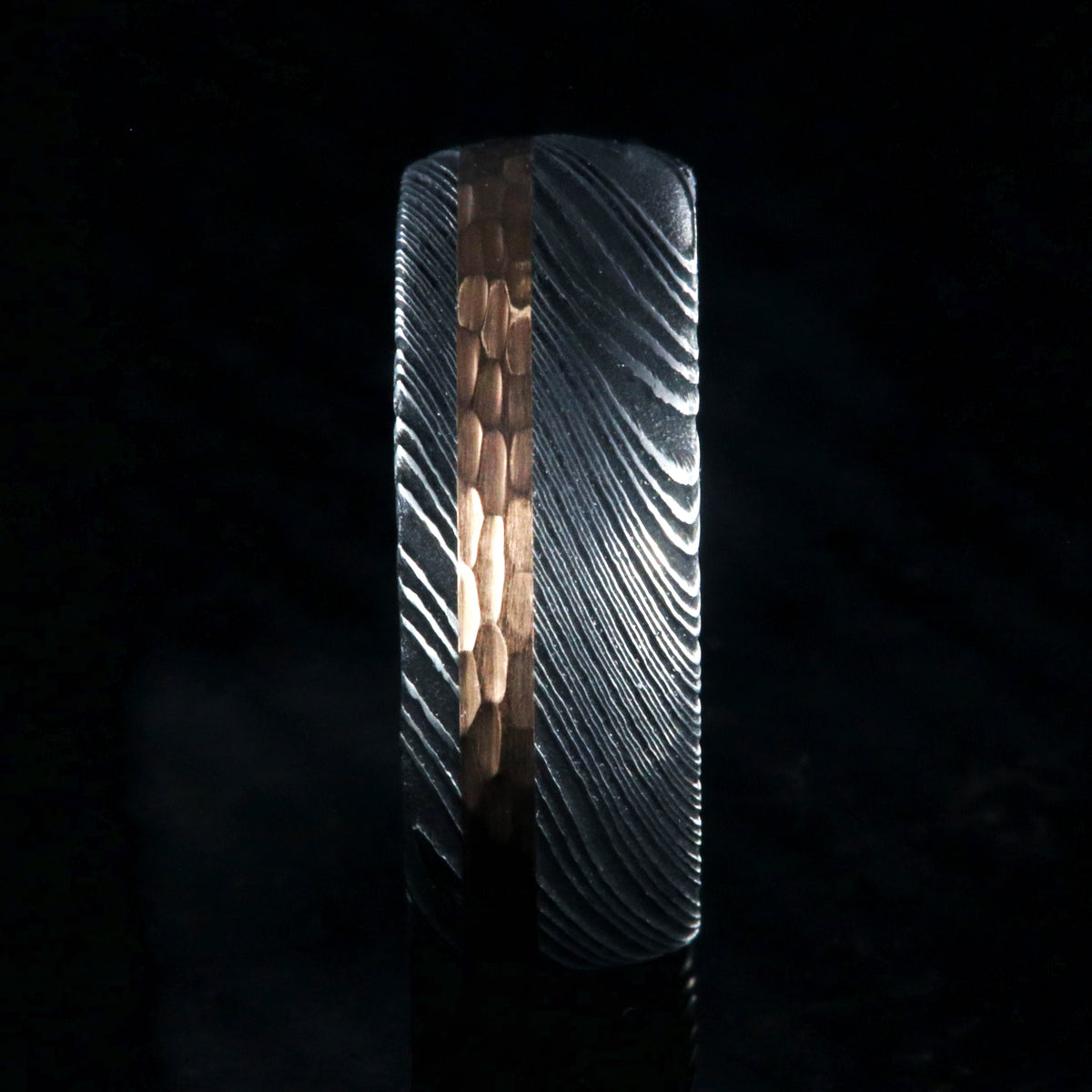 8mm wide black Damascus steel wedding band with a wide rose gold inlay with hammered finish and polished inside