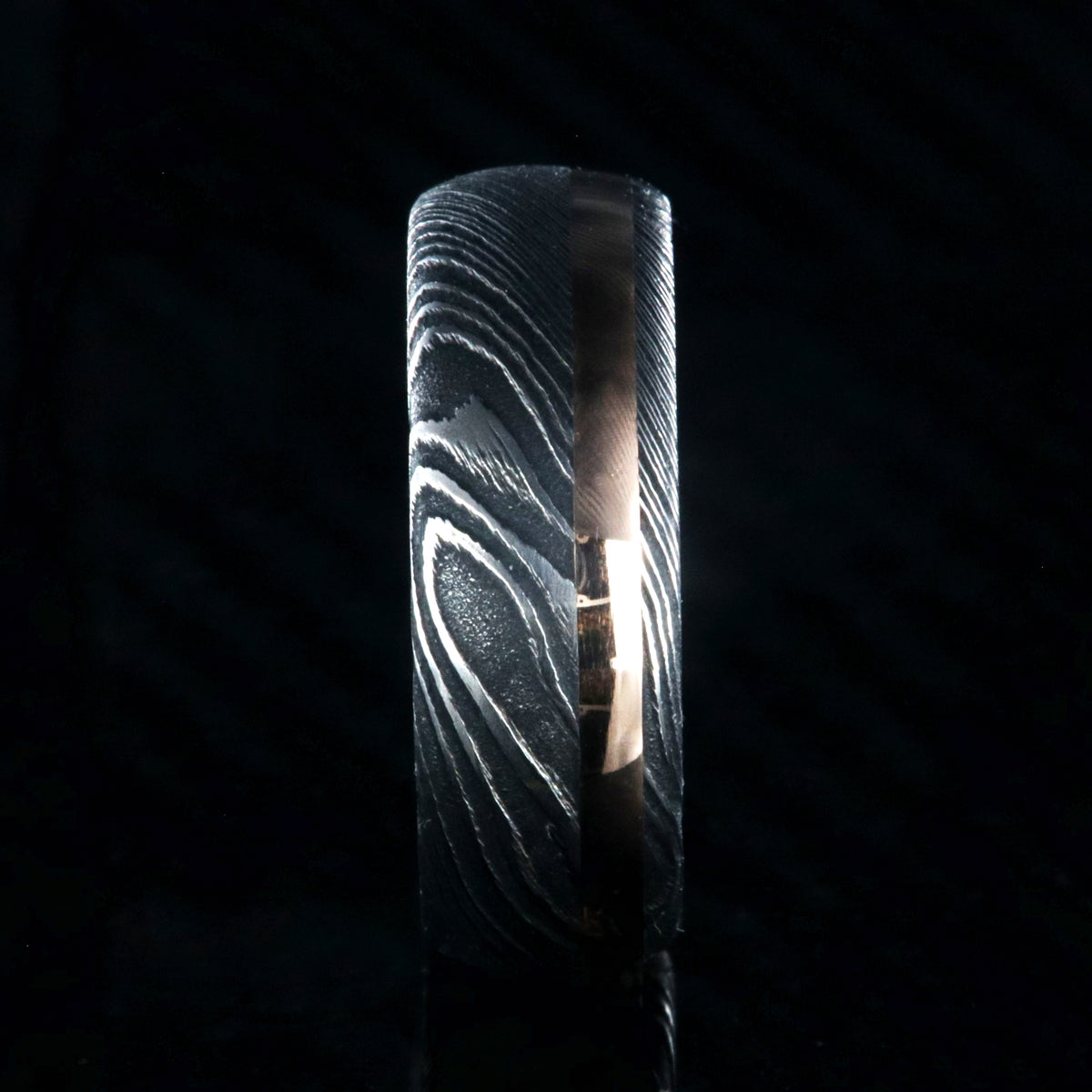 8mm wide black Damascus steel wedding band with a 2mm wide rose gold inlay and rounded profile