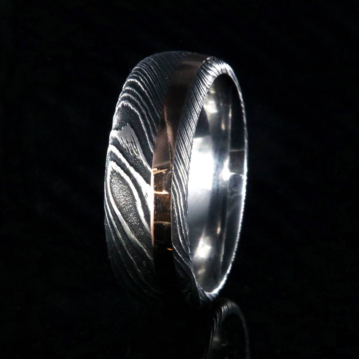 8mm wide black Damascus steel wedding band with a 2mm wide rose gold inlay and rounded profile