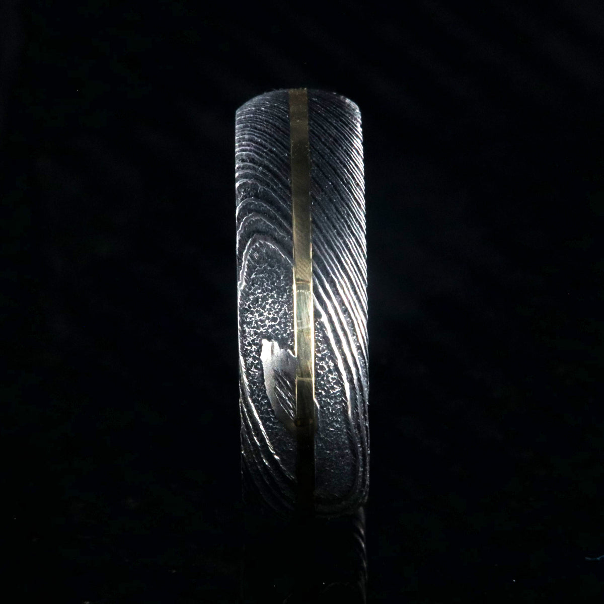 7mm wide black Damascus steel wedding band with a centered yellow gold inlay and a rounded profile