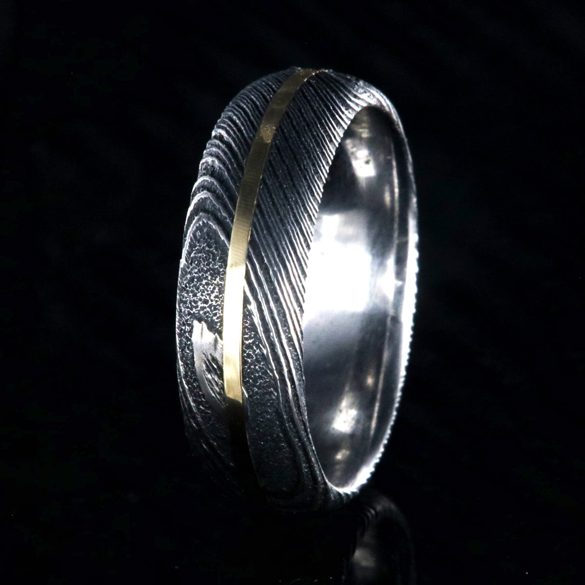 7mm wide black Damascus steel wedding band with a centered yellow gold inlay and a rounded profile
