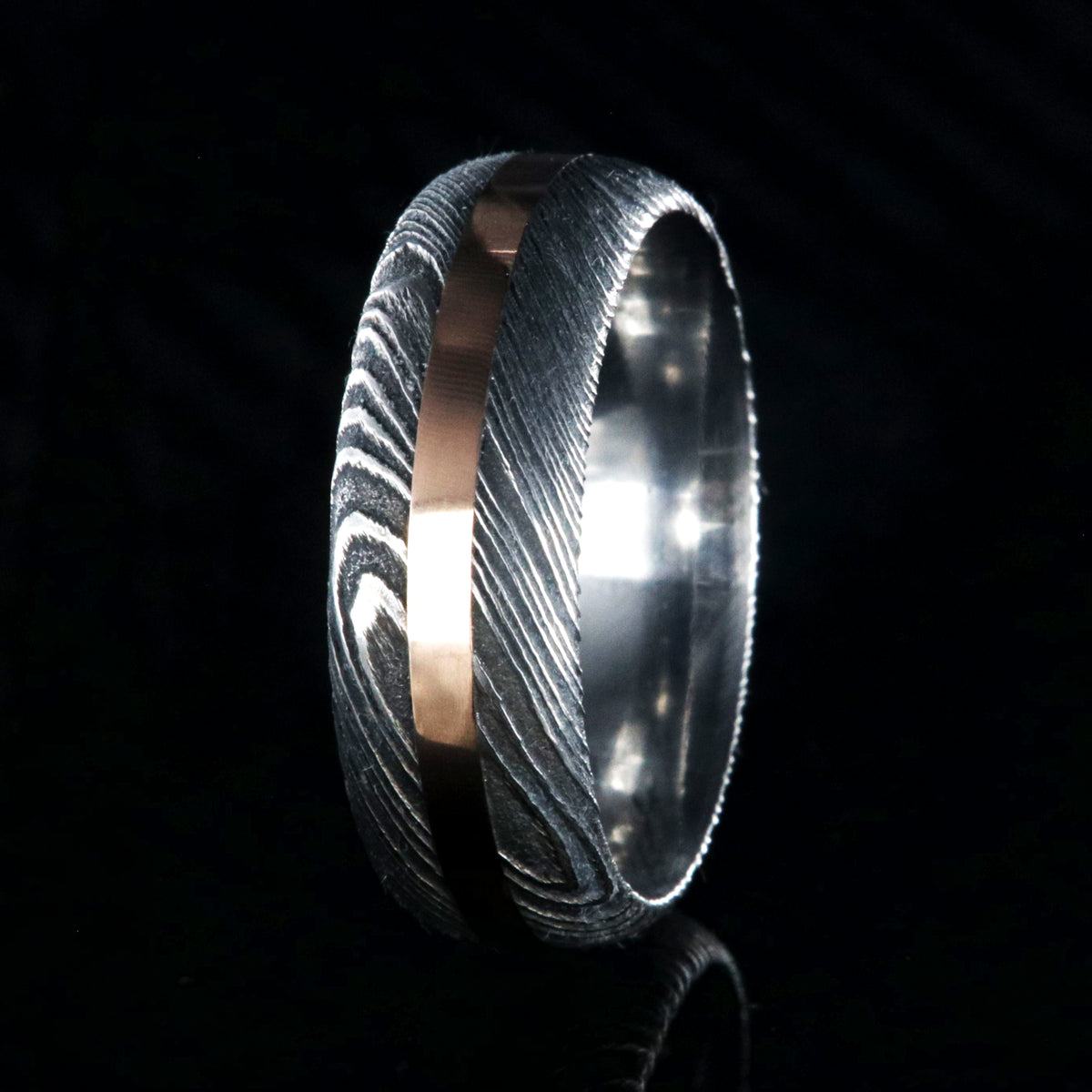 8mm wide black Damascus steel wedding band with a centered rose gold inlay and rounded profile