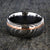 10mm wide black Damascus steel wedding band for men with two-tone pattern, an off-center rose gold inlay, and a polished inside