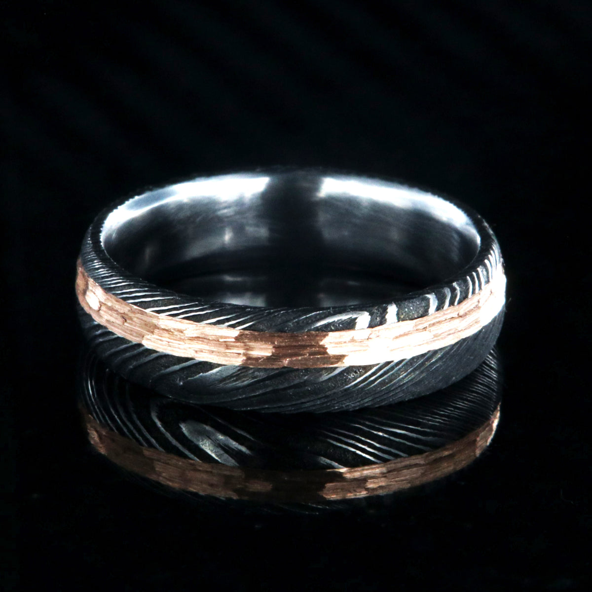 6mm wide black Damascus steel wedding band with a 2mm wide hammered rose gold inlay