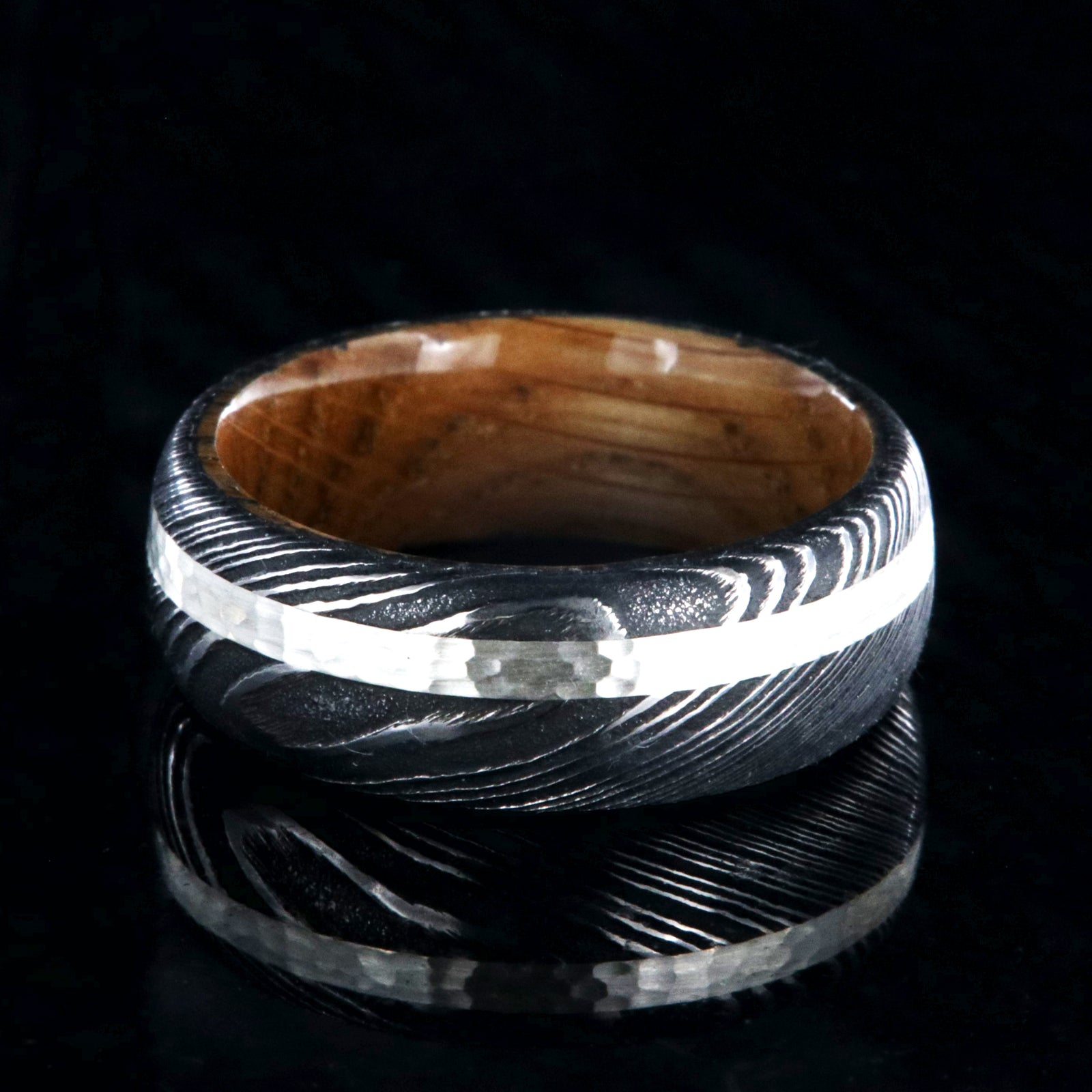 8mm wide black Damascus steel wedding band with a hammered 2mm wide sterling silver inlay and a whiskey barrel sleeve