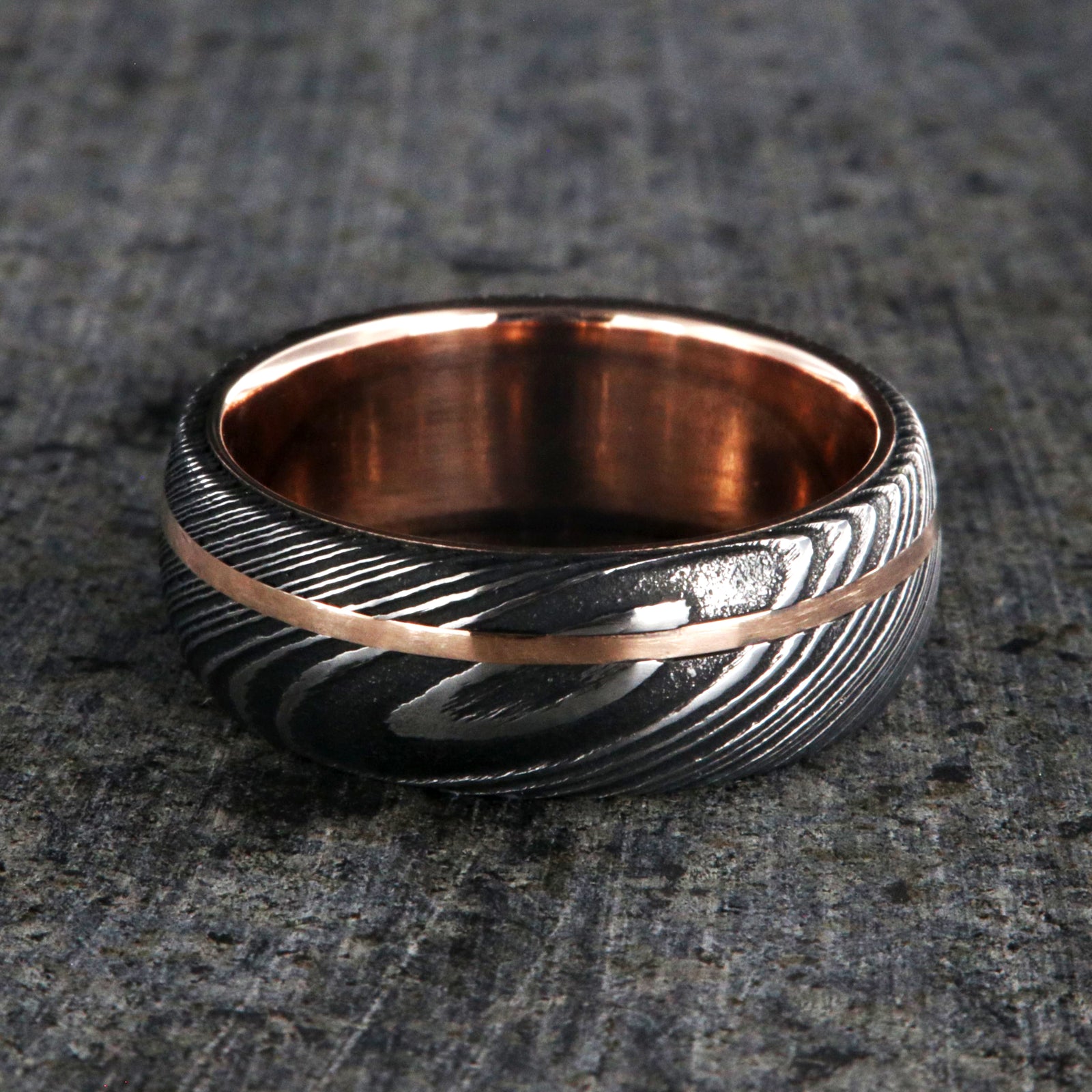 8mm wide men's wedding band made of Damascus steel with a thin off-centered rose gold inlay and solid rose gold sleeve