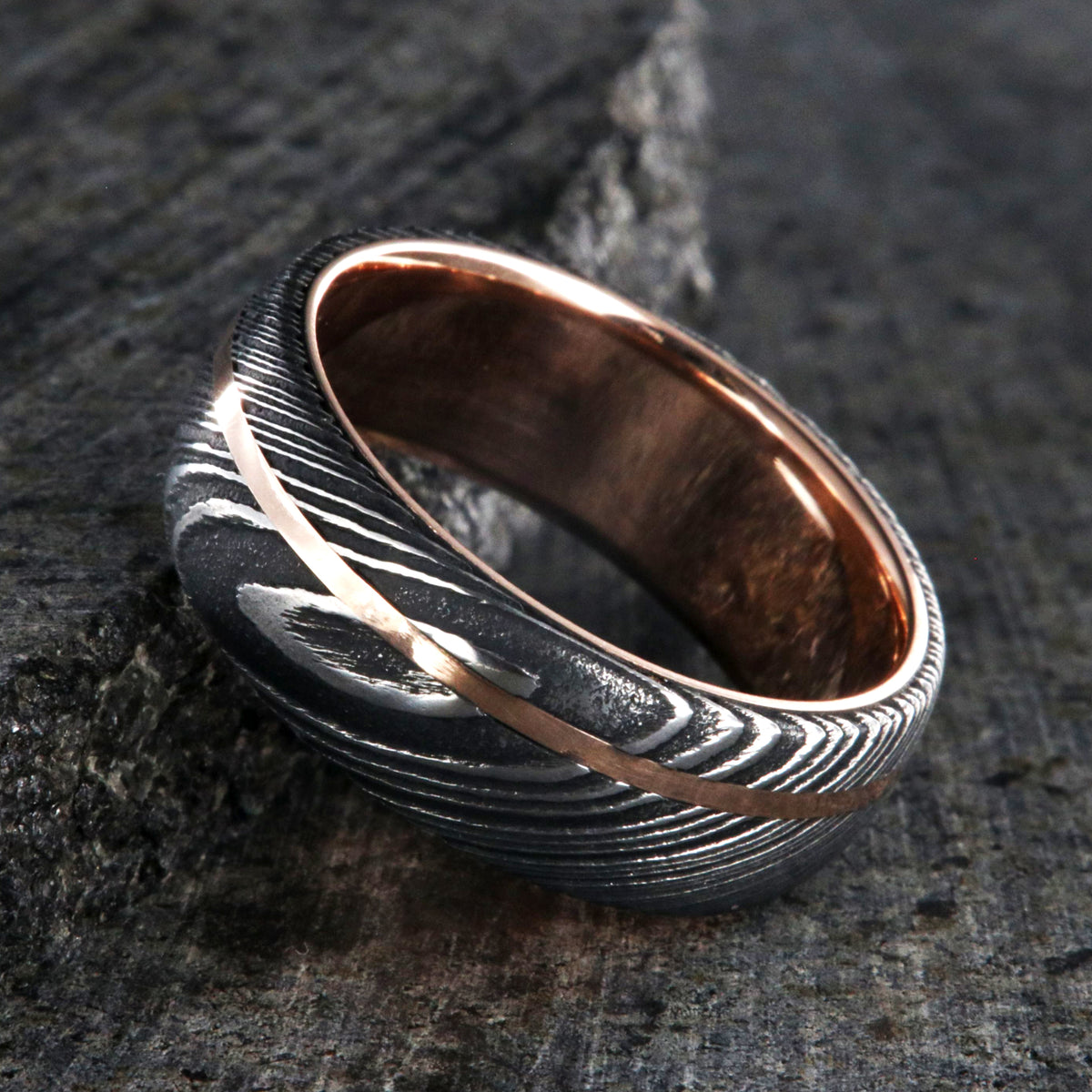 8mm wide men&#39;s wedding band made of Damascus steel with a thin off-centered rose gold inlay and solid rose gold sleeve