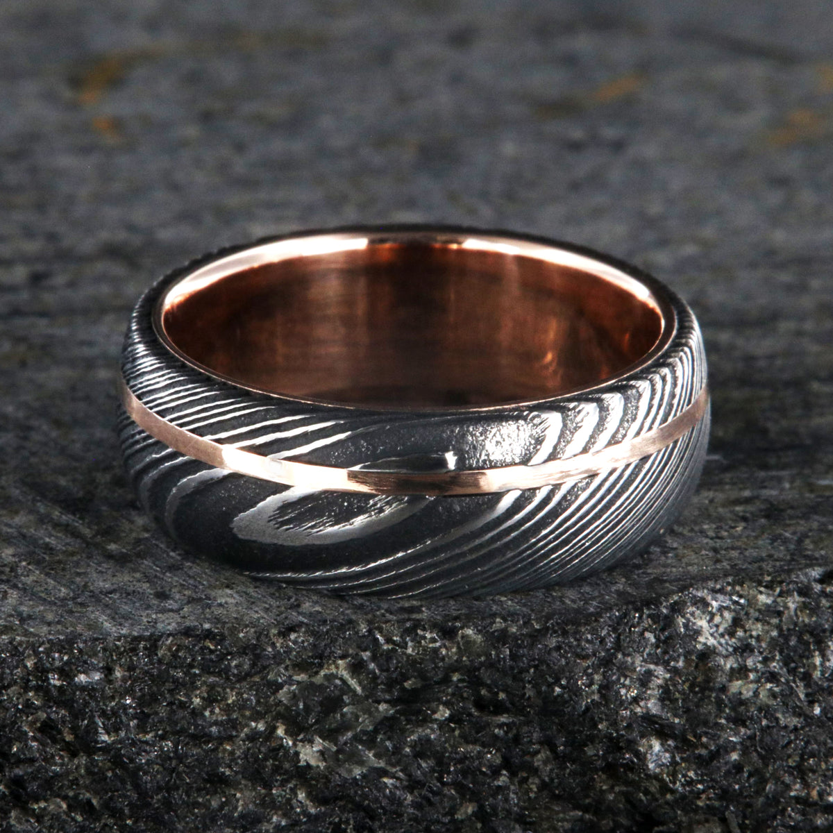 8mm wide men&#39;s wedding band made of Damascus steel with a thin off-centered rose gold inlay and solid rose gold sleeve