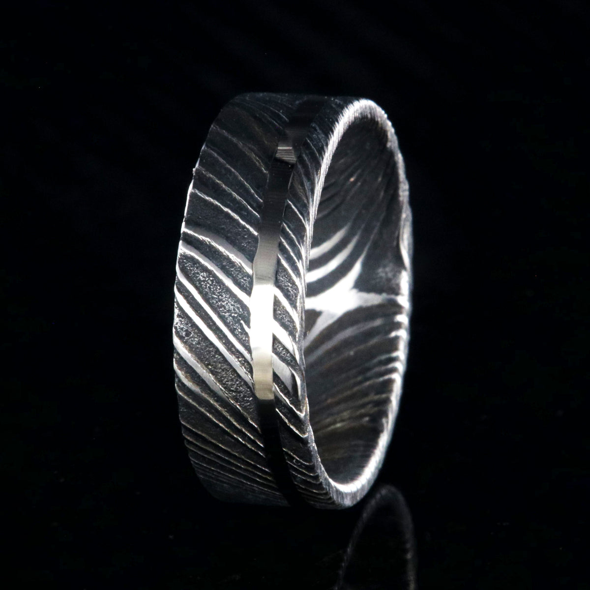 7mm wide black Damascus steel wedding ring with a white gold inlay