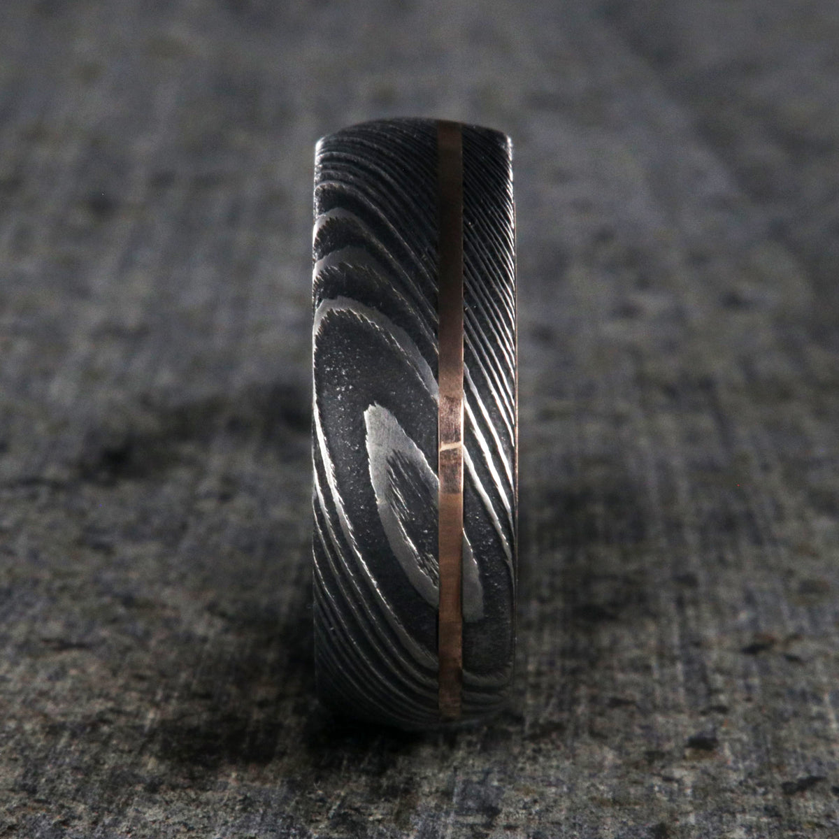 8mm wide men&#39;s wedding band made of Damascus steel with a thin off-centered rose gold inlay and solid rose gold sleeve