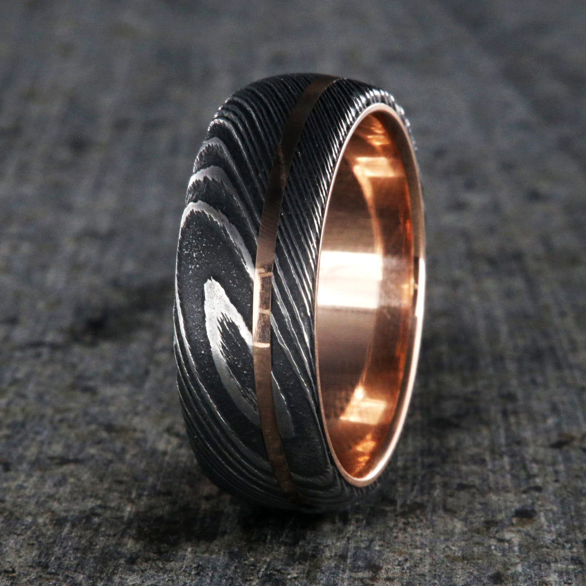8mm wide men&#39;s wedding band made of Damascus steel with a thin off-centered rose gold inlay and solid rose gold sleeve