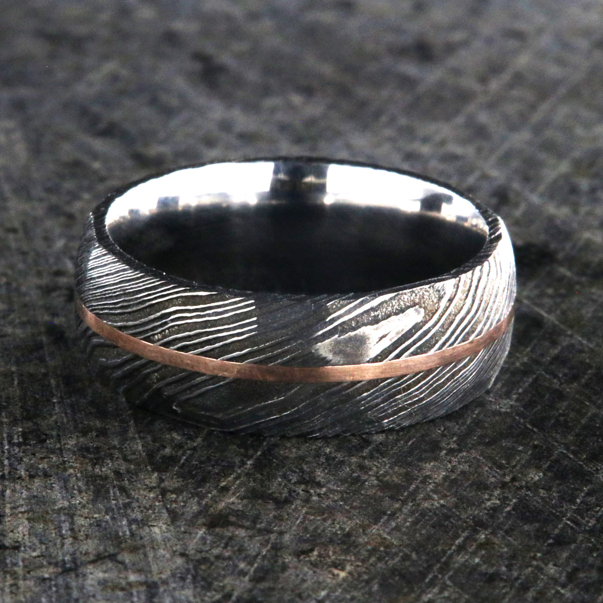 8mm wide black Damascus steel ring with two-tone pattern with a centered rose gold inlay and a big hammered finish