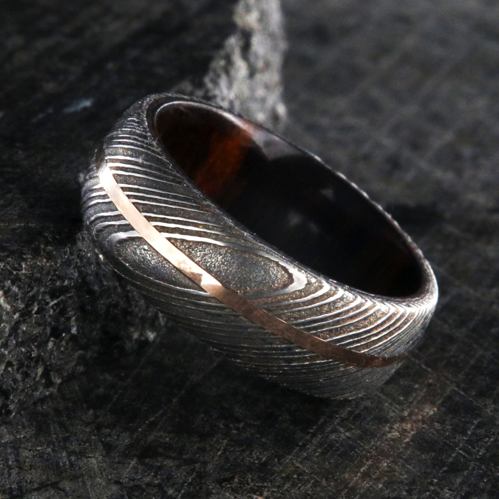 7mm wide men's Damascus steel wedding ring with a thin centered rose gold inlay and Arizona ironwood sleeve
