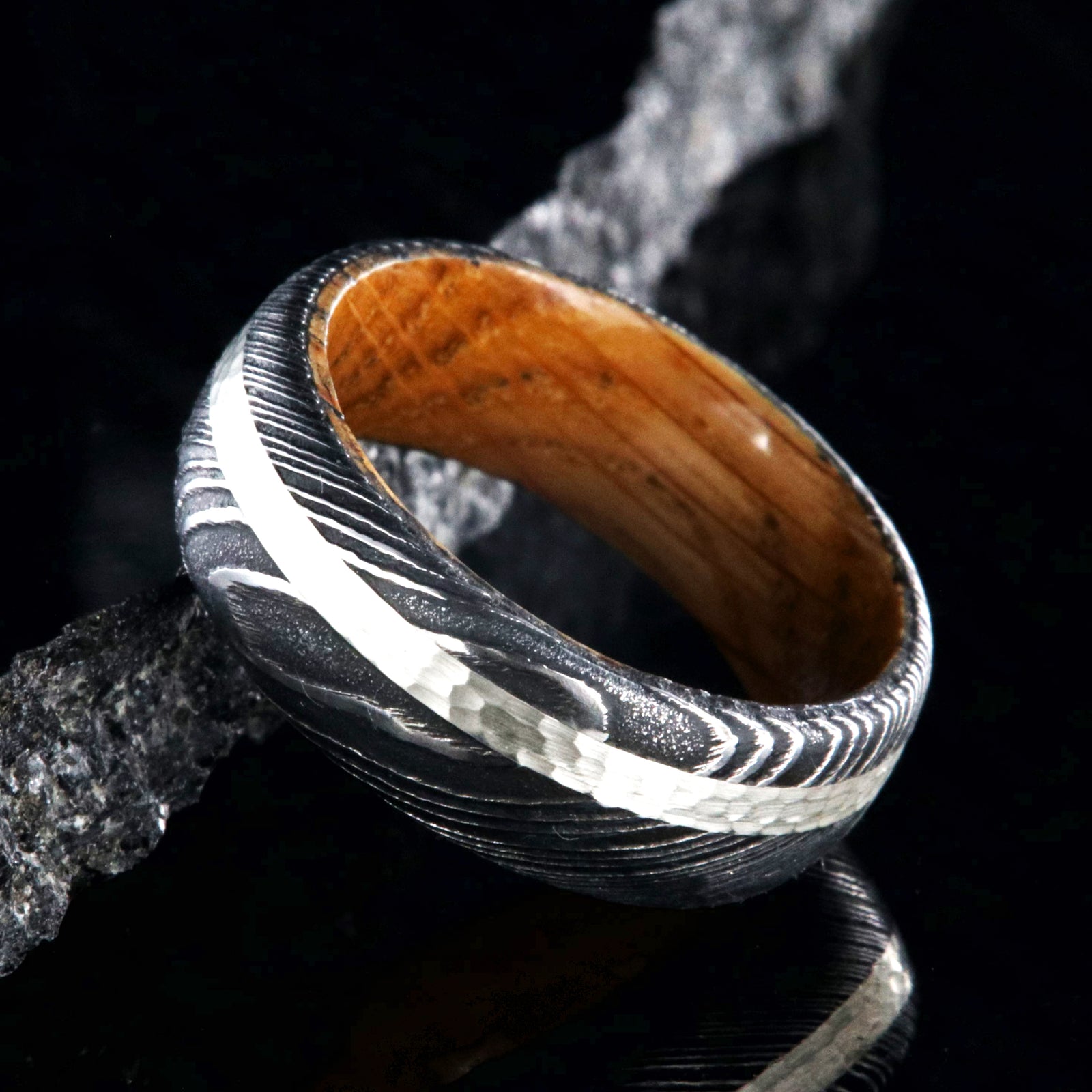 8mm wide black Damascus steel wedding band with a hammered 2mm wide sterling silver inlay and a whiskey barrel sleeve