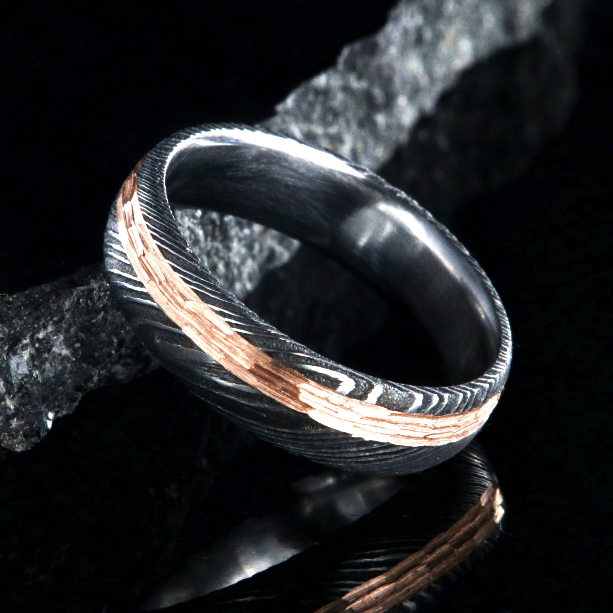 6mm wide black Damascus steel wedding band with a 2mm wide hammered rose gold inlay
