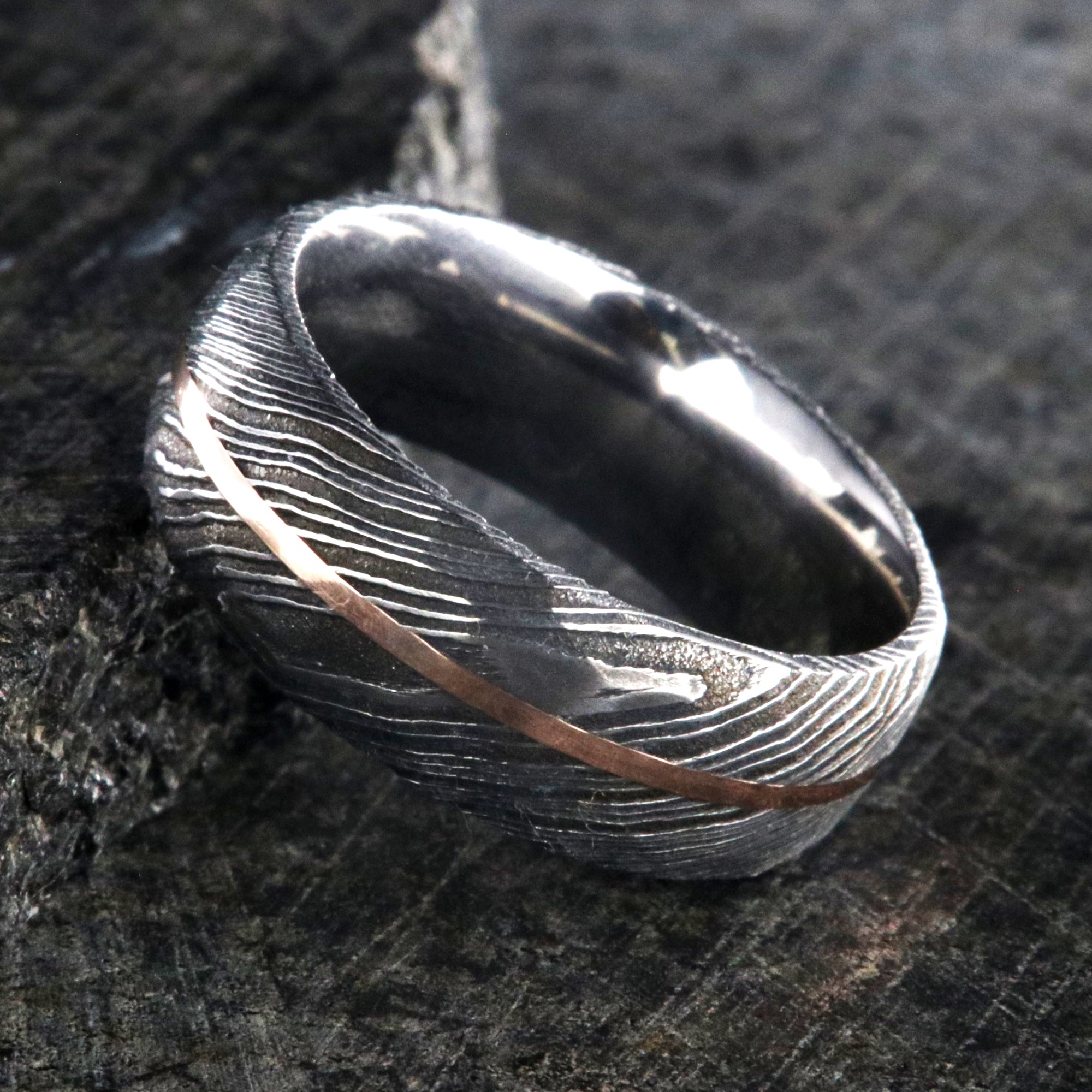 8mm wide black Damascus steel ring with two-tone pattern with a centered rose gold inlay and a big hammered finish