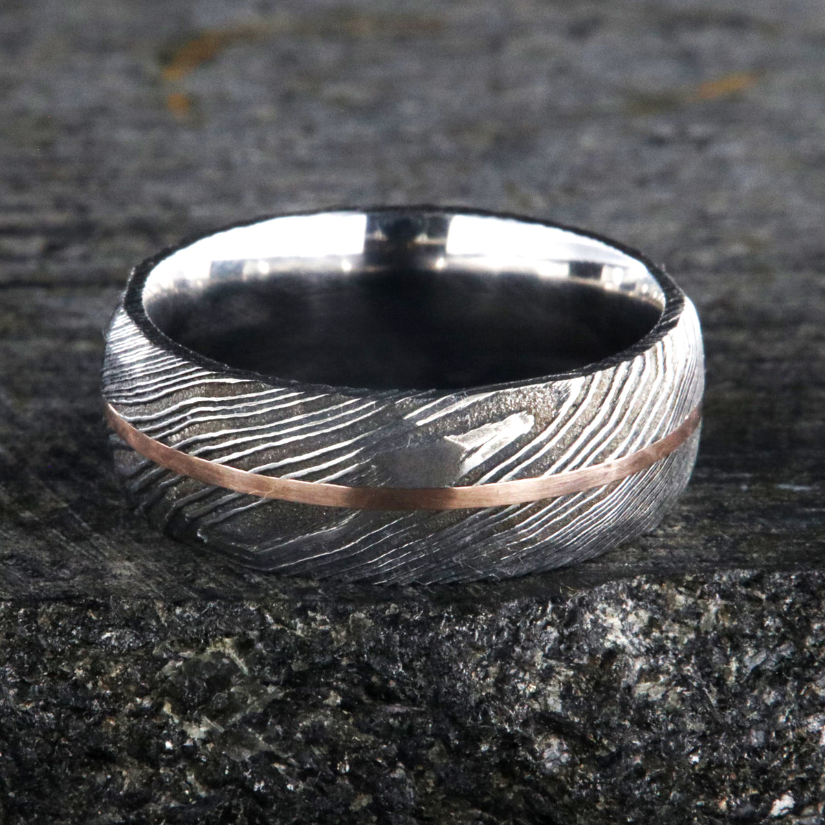 8mm wide black Damascus steel ring with two-tone pattern with a centered rose gold inlay and a big hammered finish