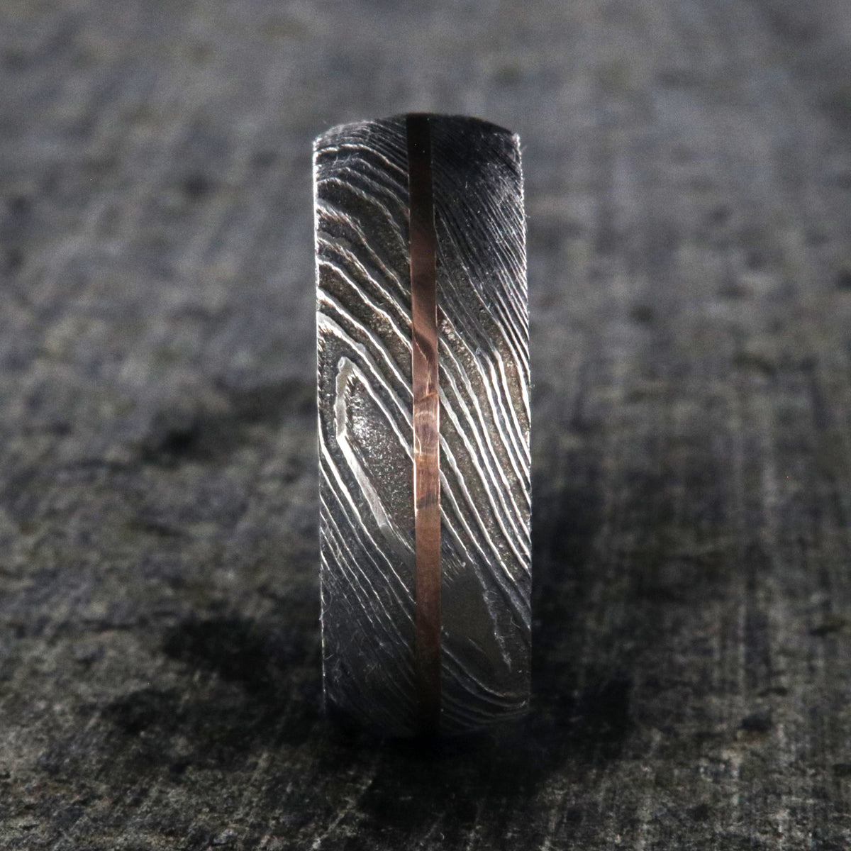 8mm wide black Damascus steel ring with two-tone pattern with a centered rose gold inlay and a big hammered finish