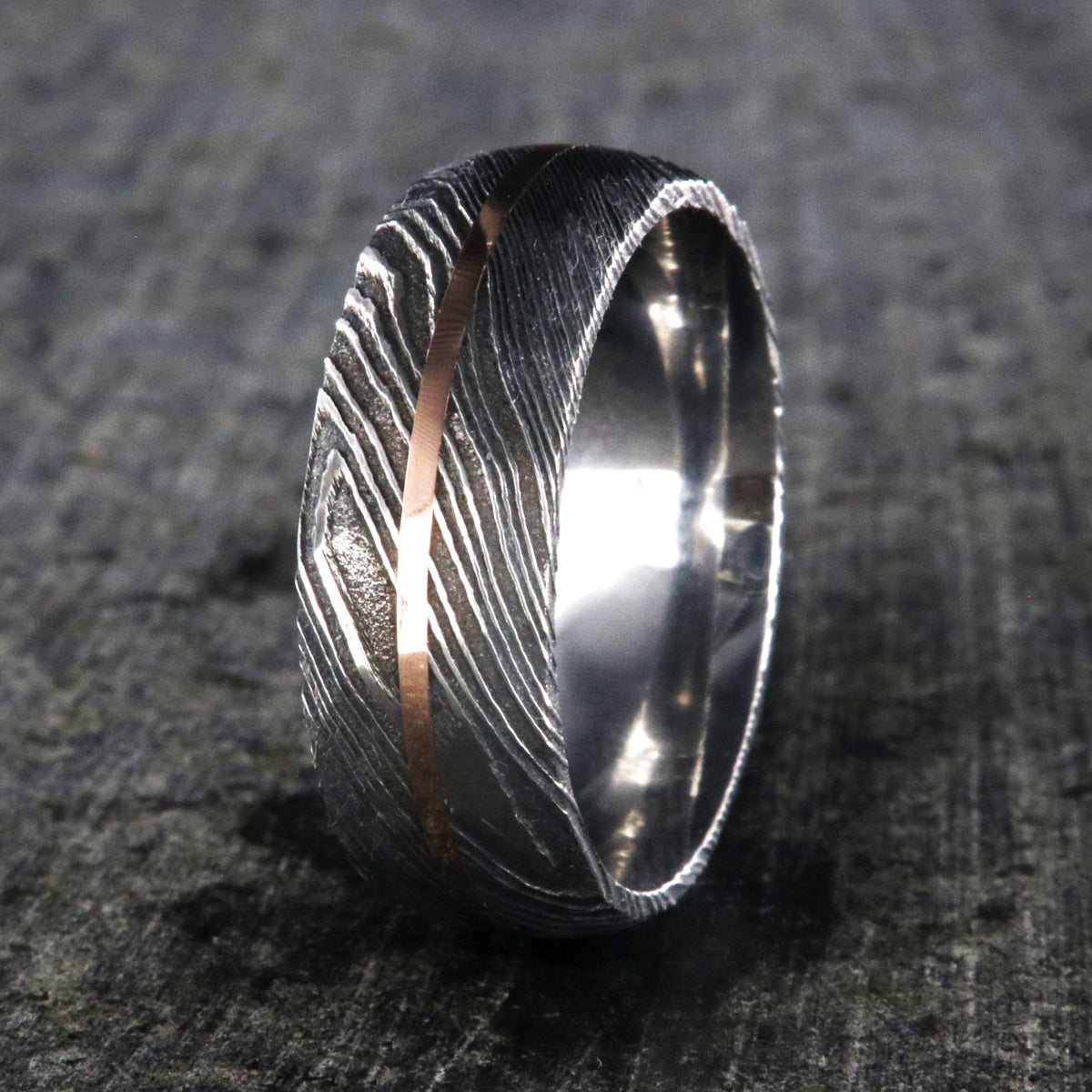8mm wide black Damascus steel ring with two-tone pattern with a centered rose gold inlay and a big hammered finish