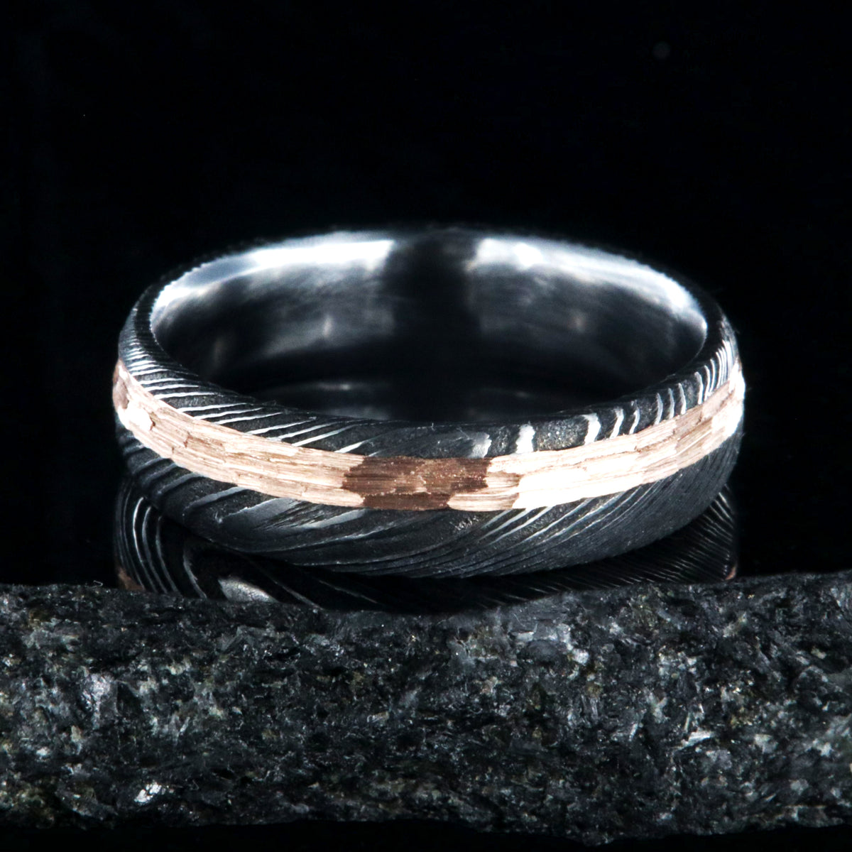 6mm wide black Damascus steel wedding band with a 2mm wide hammered rose gold inlay