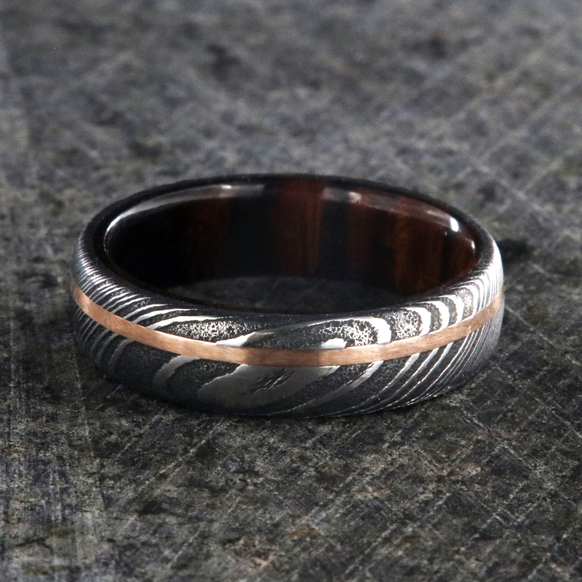 6mm wide black Damascus steel ring with off-center rose gold inlay and an Arizona ironwood sleeve