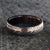 6mm wide black Damascus steel ring with off-center rose gold inlay and an Arizona ironwood sleeve