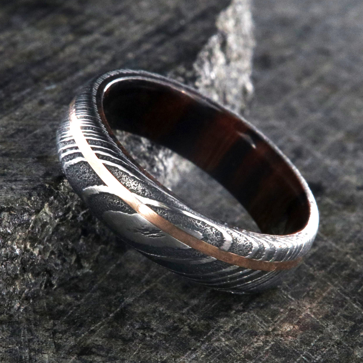 6mm wide black Damascus steel ring with off-center rose gold inlay and an Arizona ironwood sleeve