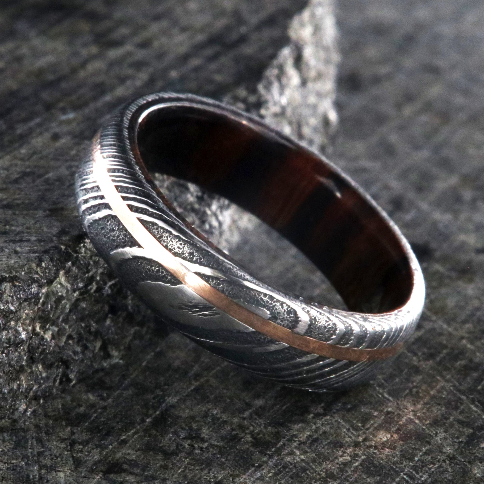 6mm wide black Damascus steel ring with off-center rose gold inlay and an Arizona ironwood sleeve