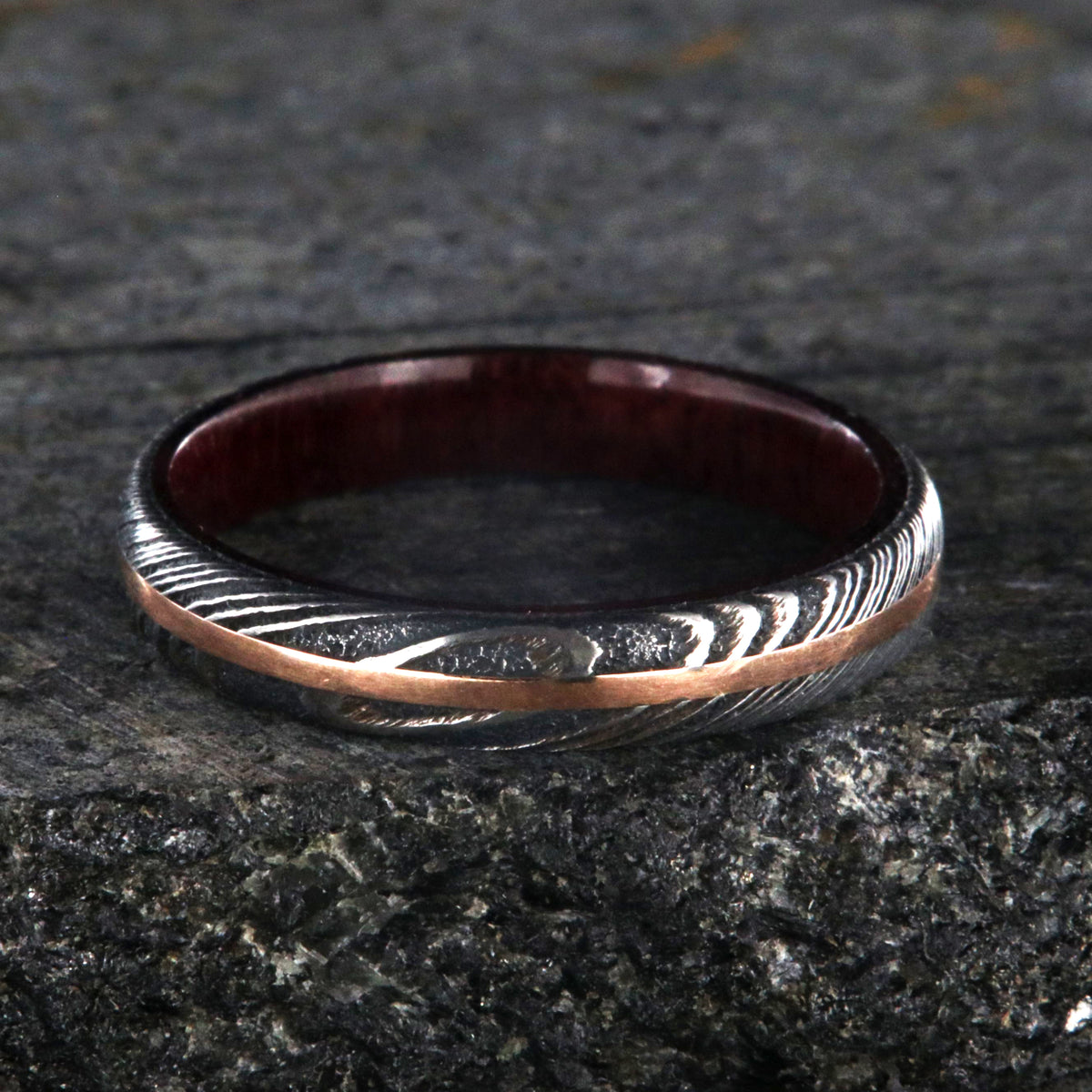 4mm wide women&#39;s wedding band made with black Damascus steel with a centered rose gold inlay and purple rain wood sleeve