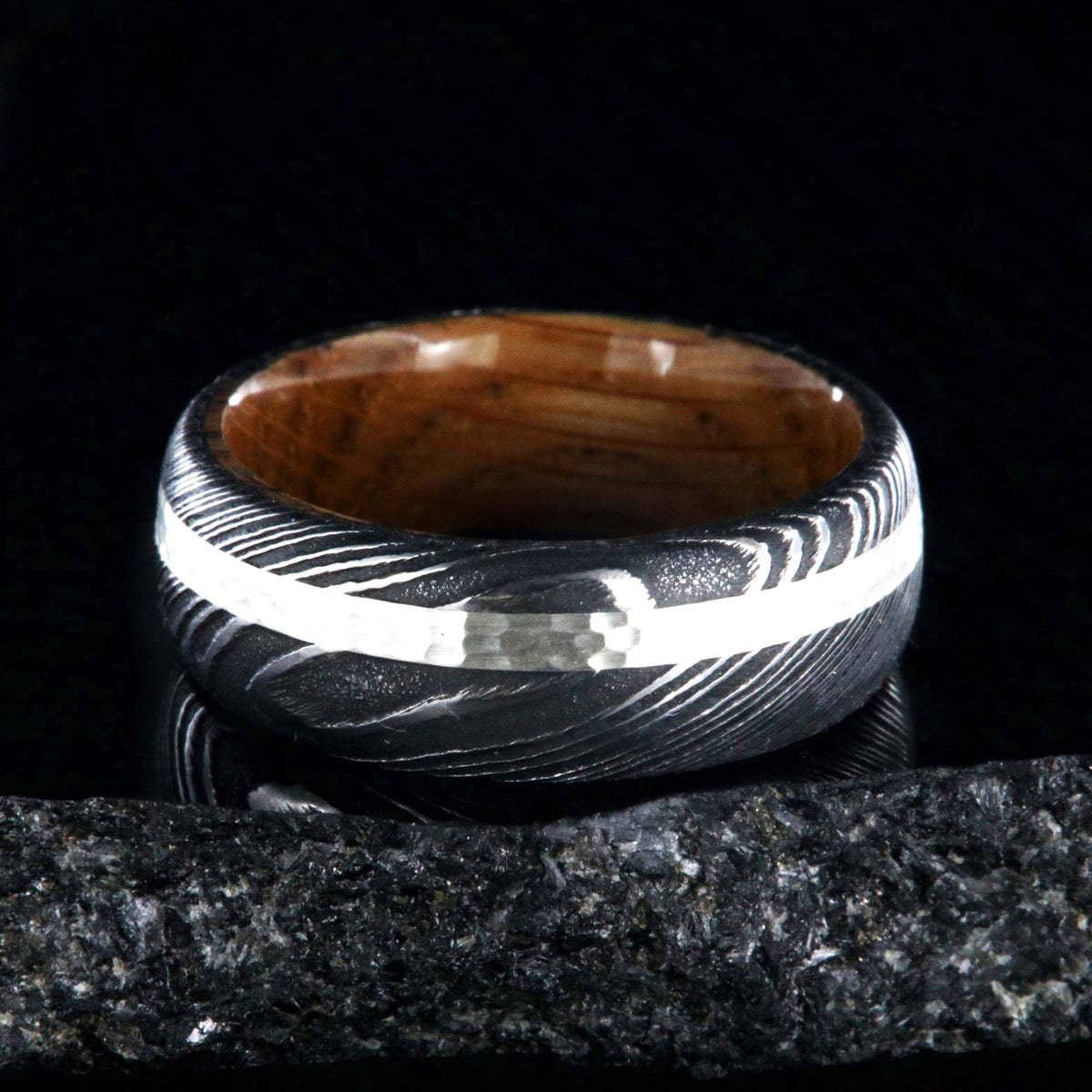 8mm wide black Damascus steel wedding band with a hammered 2mm wide sterling silver inlay and a whiskey barrel sleeve