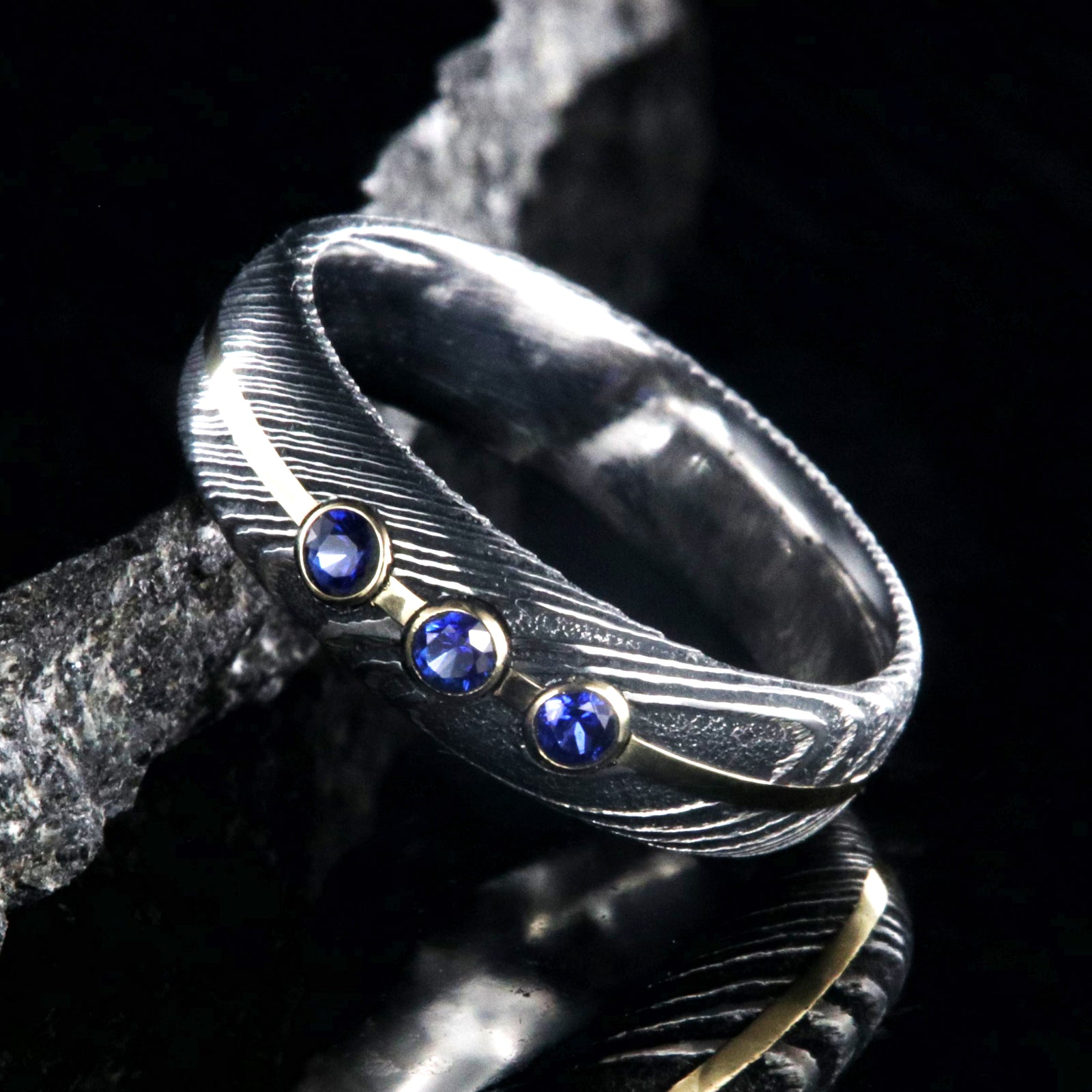 6mm wide black Damascus steel wedding band with 3 blue sapphire stone with a yellow gold center inlay