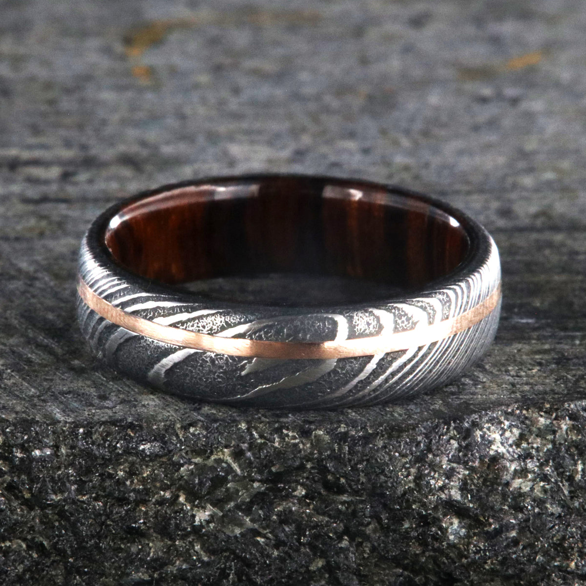 6mm wide black Damascus steel ring with off-center rose gold inlay and an Arizona ironwood sleeve