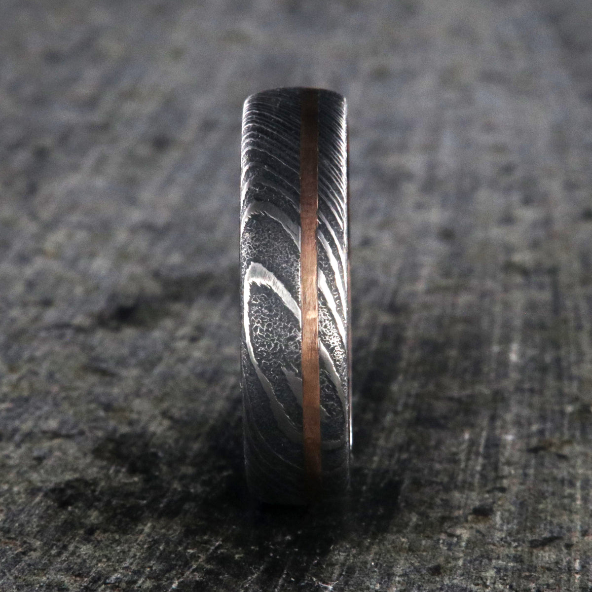 6mm wide black Damascus steel ring with off-center rose gold inlay and an Arizona ironwood sleeve